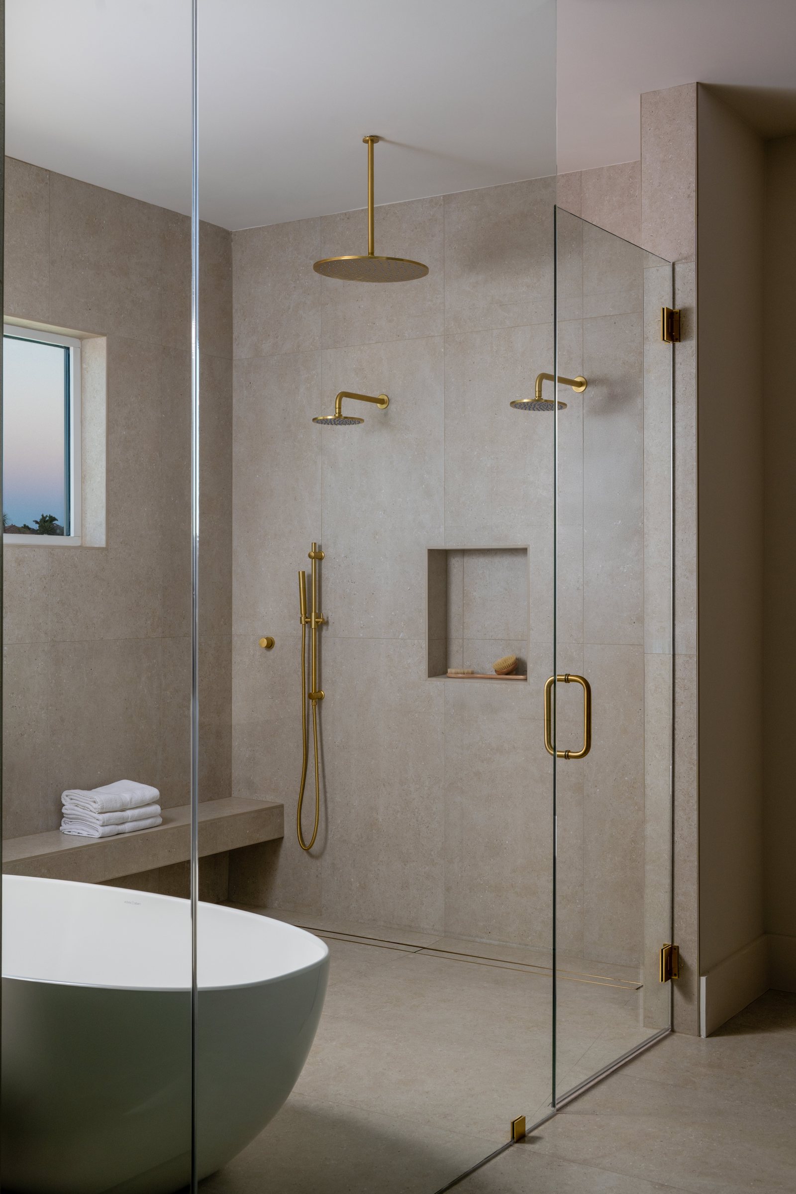 Stone shower with dual gold rain heads and frameless glass